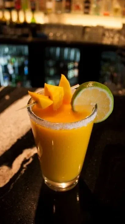 Vibrant yellow-orange blended drink, mango and lime, on a bar.