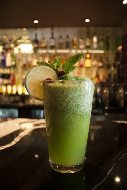 Frothy green drink in glass, garnished with lime, mint, berries.
