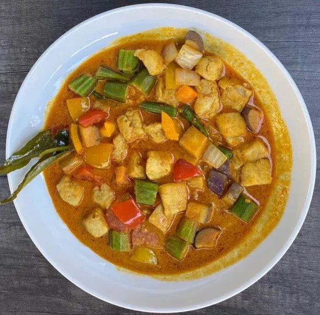 Overhead shot of reddish-orange curry with mixed vegetables and protein.