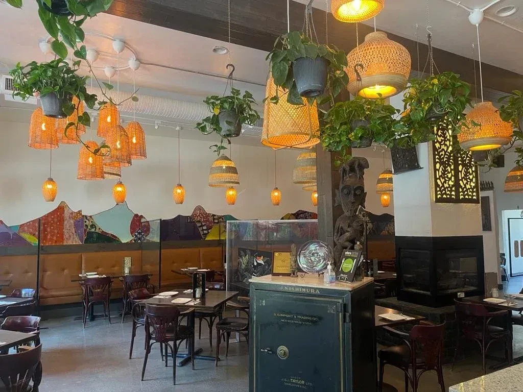 Bohemian restaurant interior with lush plants, woven lights, and vibrant mural.