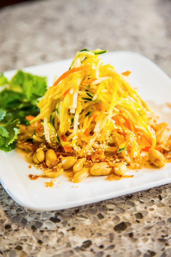 Vibrant julienned vegetable salad with peanuts, sesame seeds on a white plate.