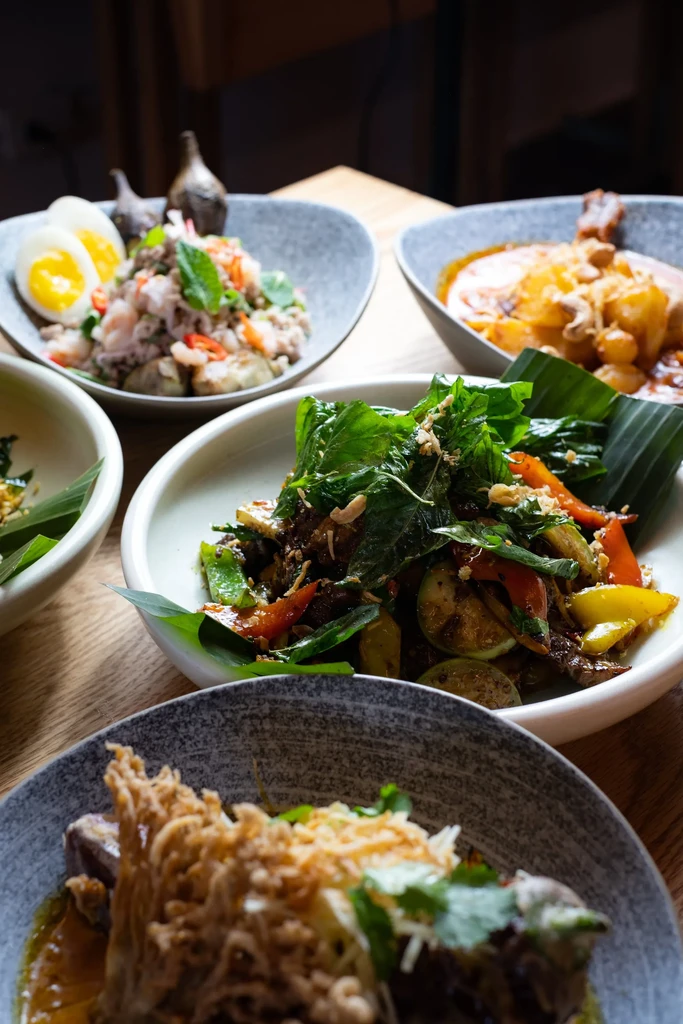 Overhead view of colorful Asian dishes on a light wooden table.