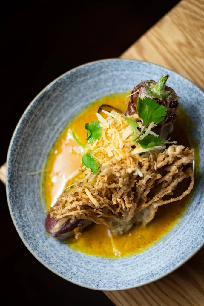 Stuffed vegetable in yellow sauce, topped with crispy strands and herbs.