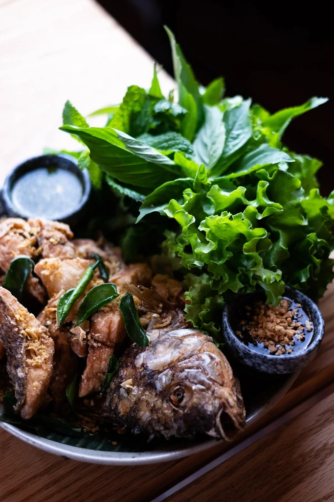 Crispy deep-fried fish, cut with head, served with greens and sauces.