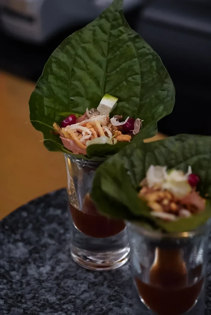 Two Miang Kham leaf cups with colorful fillings in shot glasses.