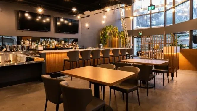 Interior of a modern restaurant bar with dining tables and large windows.