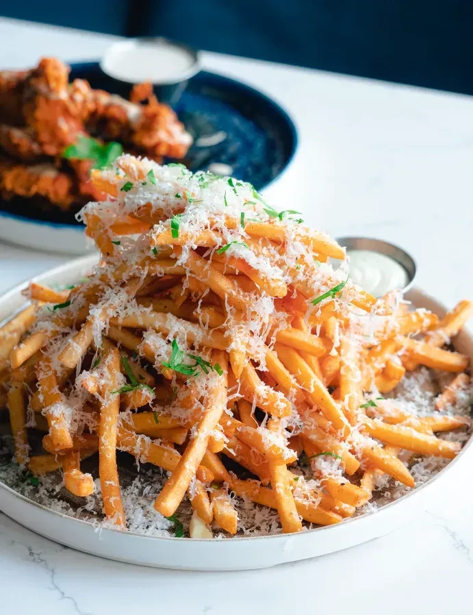 Golden-brown french fries topped with white cheese and green herbs.