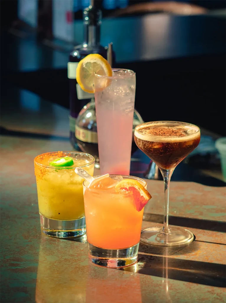 Four unique garnished cocktails in different glasses on a bar.