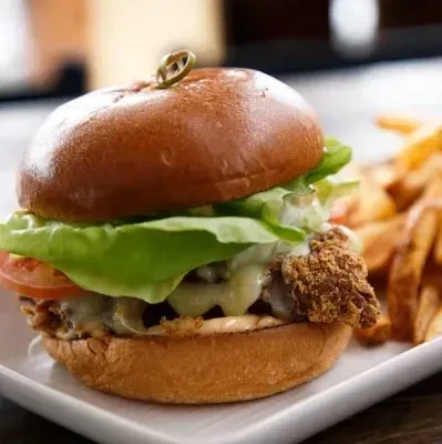 Gourmet crispy chicken burger with fries on a white plate.