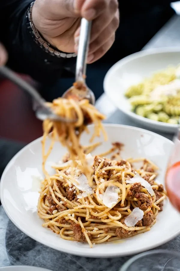 Person's hands lifting spaghetti bolognese garnished with Parmesan.