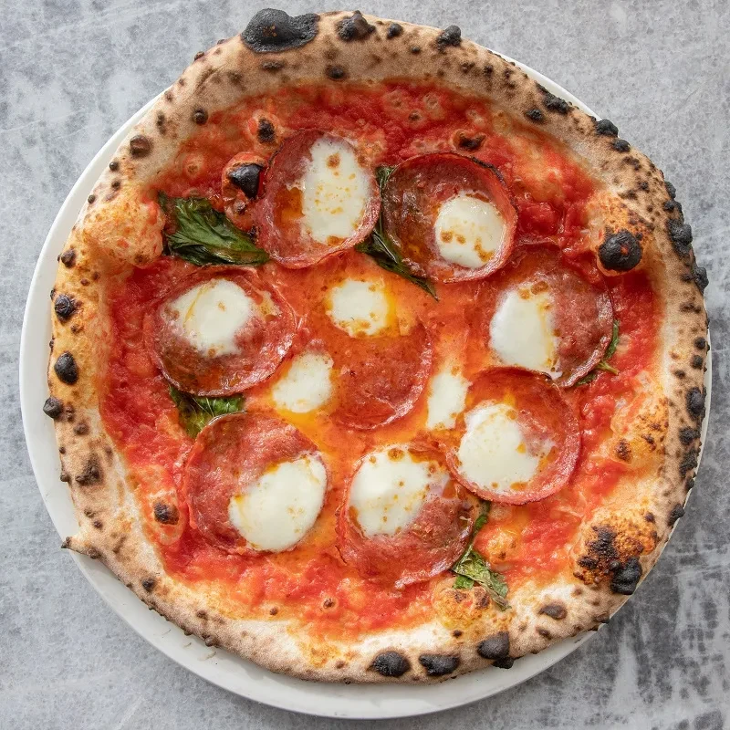 Neapolitan pizza with charred crust, pepperoni, mozzarella, and fresh basil.