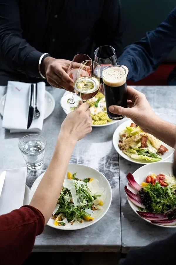 Overhead view of hands clinking drinks at a dinner table with food.