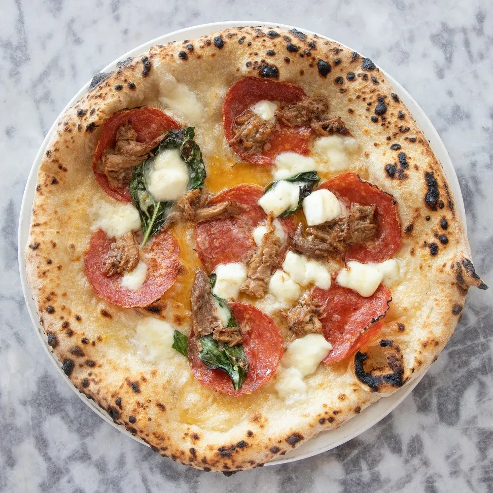 Charred Neapolitan pizza with pepperoni, mozzarella, braised meat, and fresh basil.