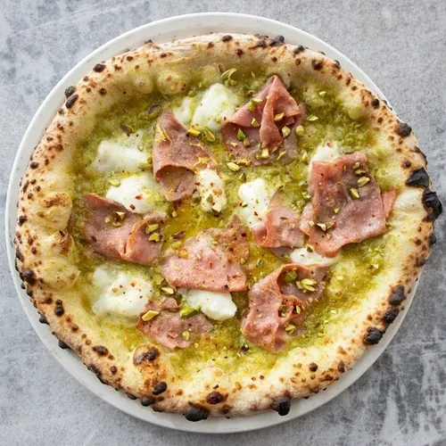 Neapolitan pizza with green pesto, melted cheese, cured meat, and pistachios.