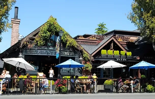 Busy outdoor patios of two establishments, ivy, umbrellas, under blue sky.