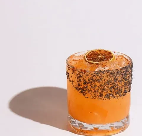 Vibrant orange cocktail in a faceted glass with a dark seasoned rim.