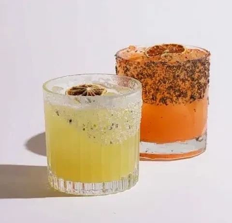 Two colorful cocktails with citrus garnishes and unique rims on white.