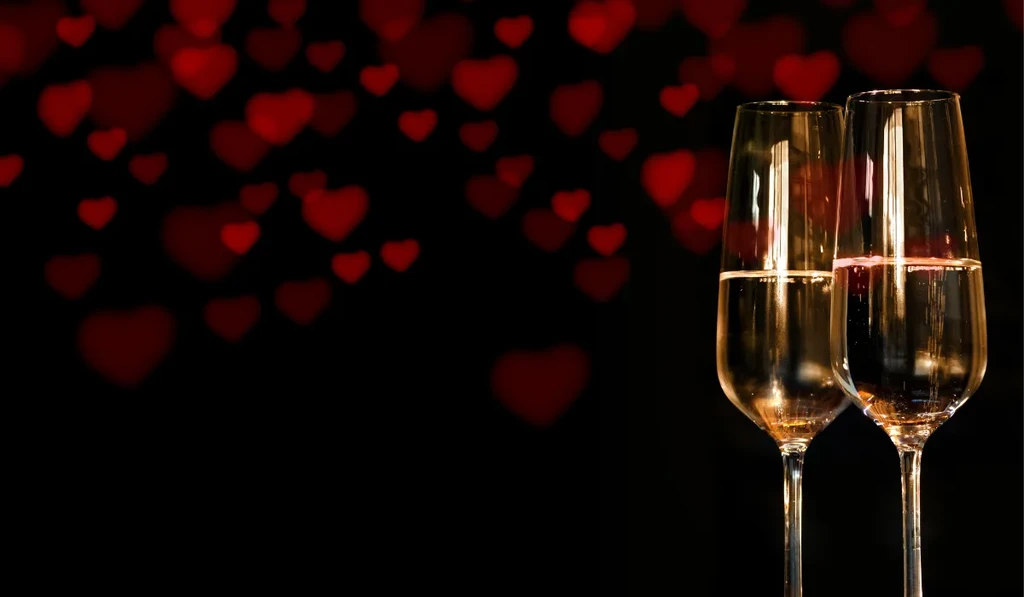 Two champagne flutes, sparkling drink, out-of-focus red heart lights.