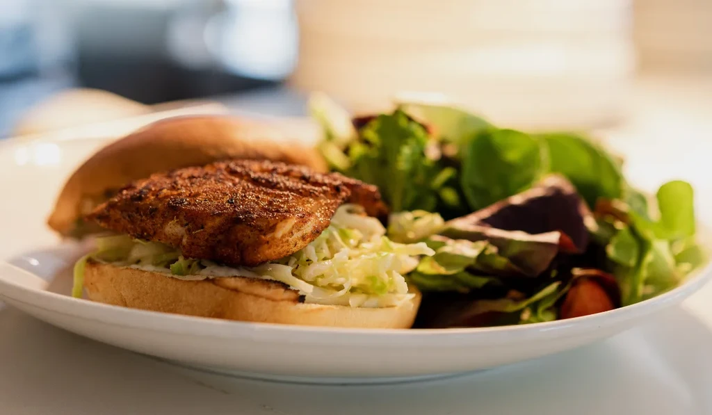 A grilled protein sandwich with coleslaw and a mixed green salad.