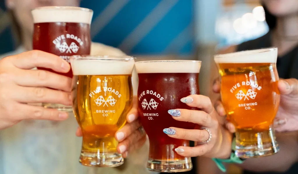 Four hands toast two dark and two light Five Roads beers.