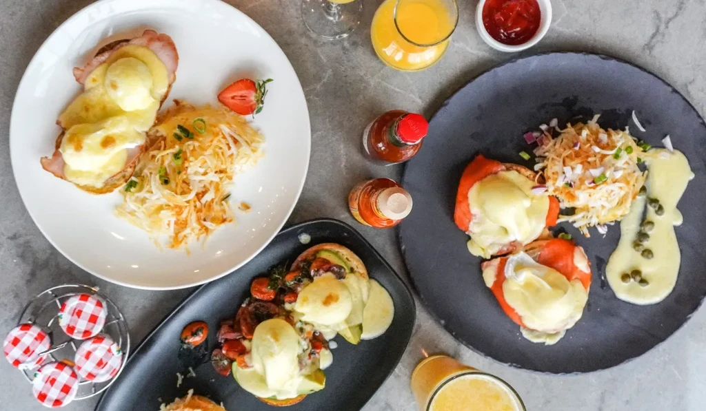 Overhead brunch spread with Eggs Benedict, avocado toast, and orange juice.