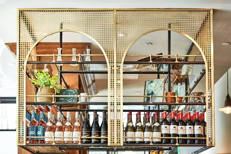 Gold metal shelving unit with arched openings displays wine and decor.