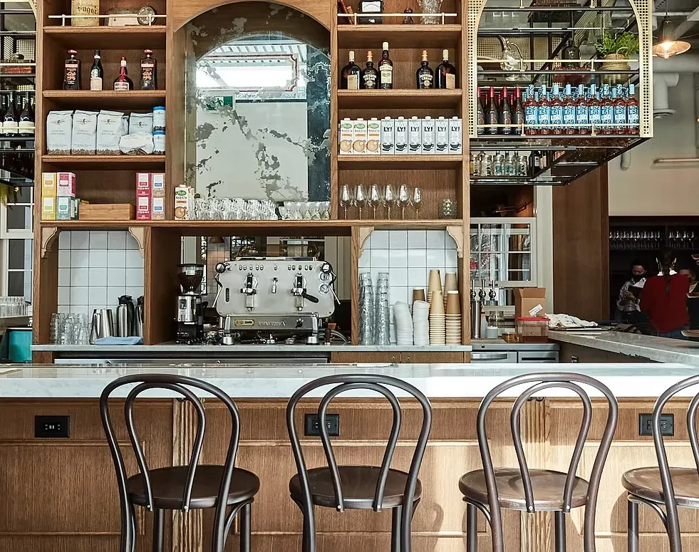 Modern cafe bar with marble counter, elaborate wooden shelving, and espresso machine.
