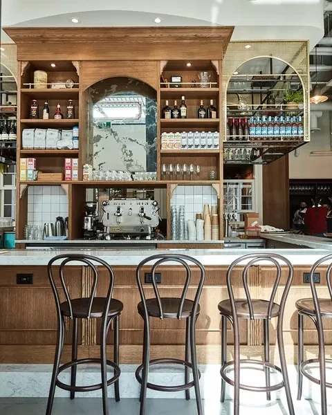 Bar counter with espresso machine, marble top, wooden shelves and stools.