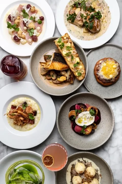 Eight artfully plated gourmet dishes and two cocktails on a marble surface.