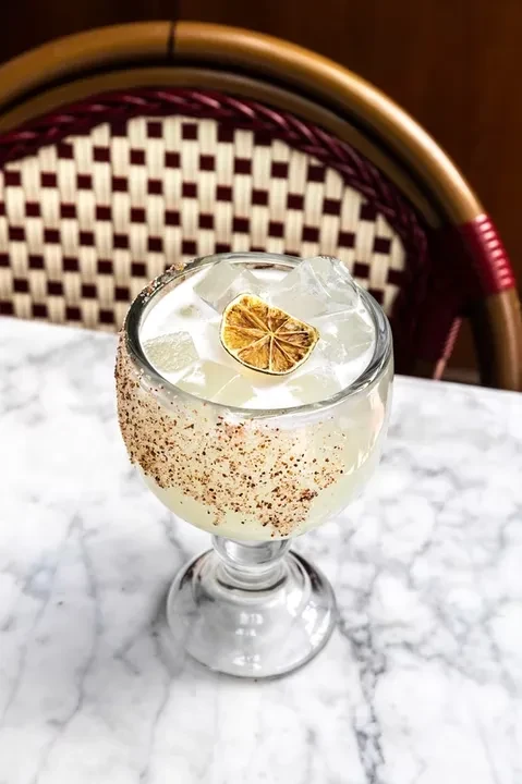 A light cocktail with ice, dried citrus, and a dark granular rim.