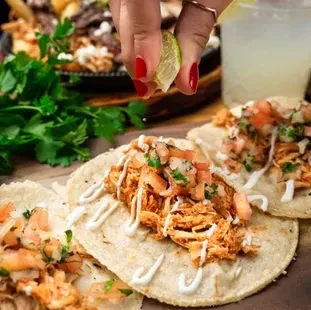 Close-up of chicken tacos with pico de gallo; hand squeezes lime.