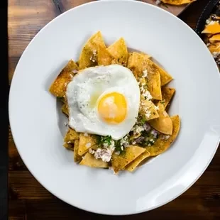 Close-up chilaquiles with green salsa, cheese, herbs, and sunny-side-up egg.