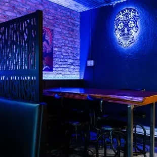 Restaurant interior with blue-lit sugar skull, live-edge table, and metal stools.