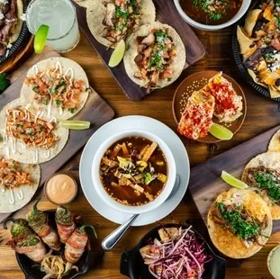 Overhead view: Tacos, nachos, soup, and drinks on a wooden table.