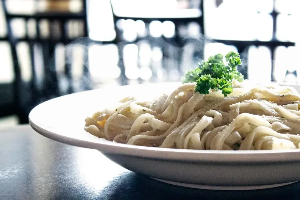 Steaming pasta topped with cheese and parsley in a white bowl.