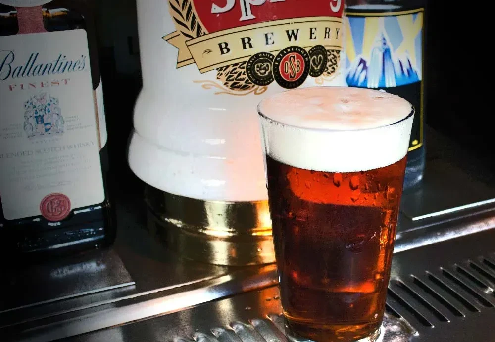 Cold beer glass on bar, with Scotch and a brewery tap.