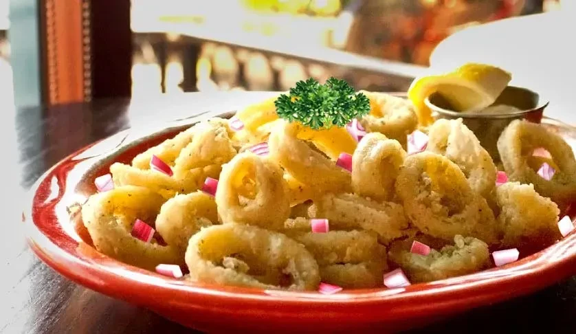 Golden-brown fried rings in bowl with parsley, red onion, lemon sauce.