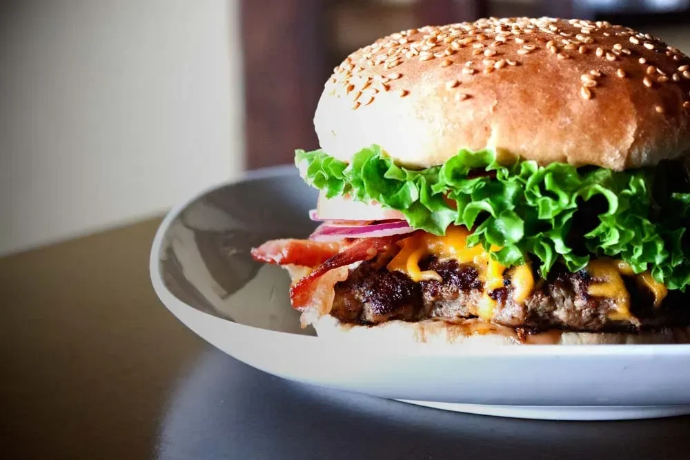 Stacked burger with sesame bun, beef patty, bacon, cheese, lettuce, onion.