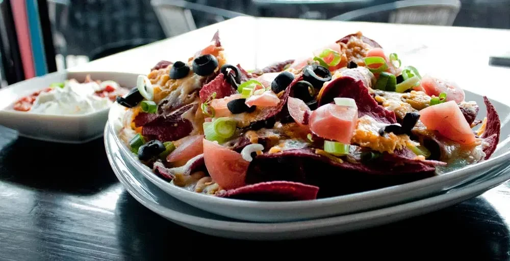 Purple sweet potato nachos with cheese, olives, tomatoes, and green onions.