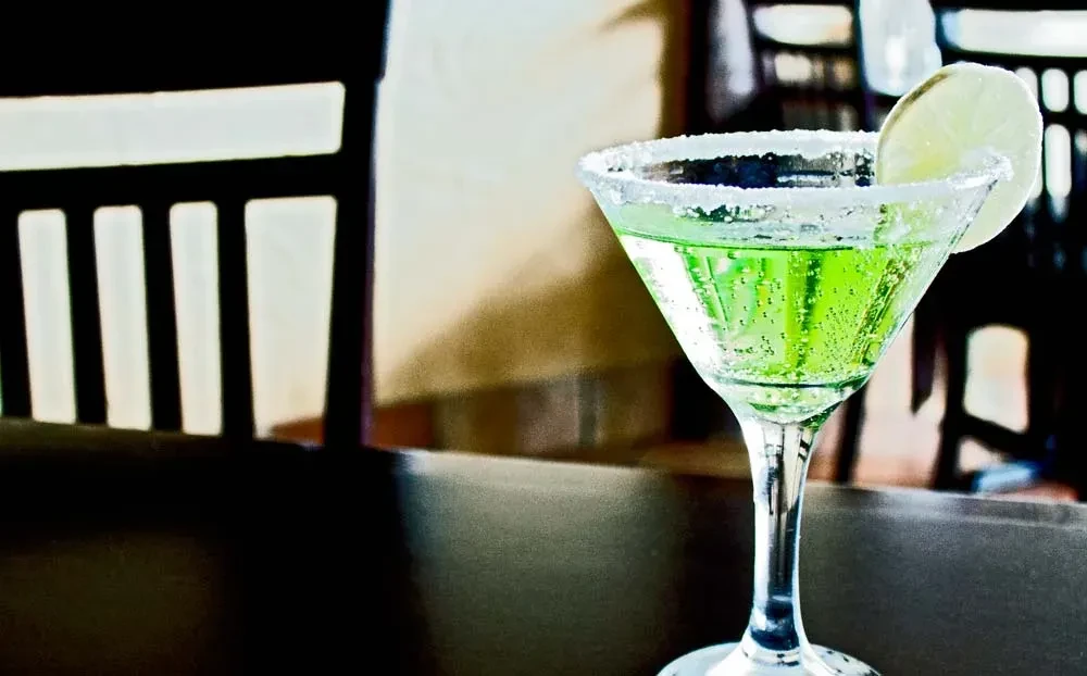Green cocktail in martini glass with salted rim and lime.