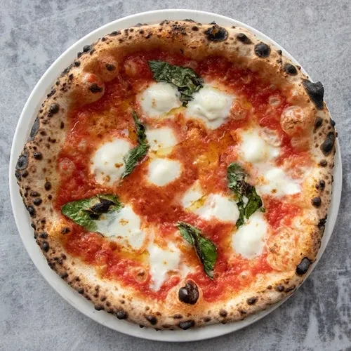 Classic Neapolitan Margherita pizza with red sauce, mozzarella, basil, charred crust.