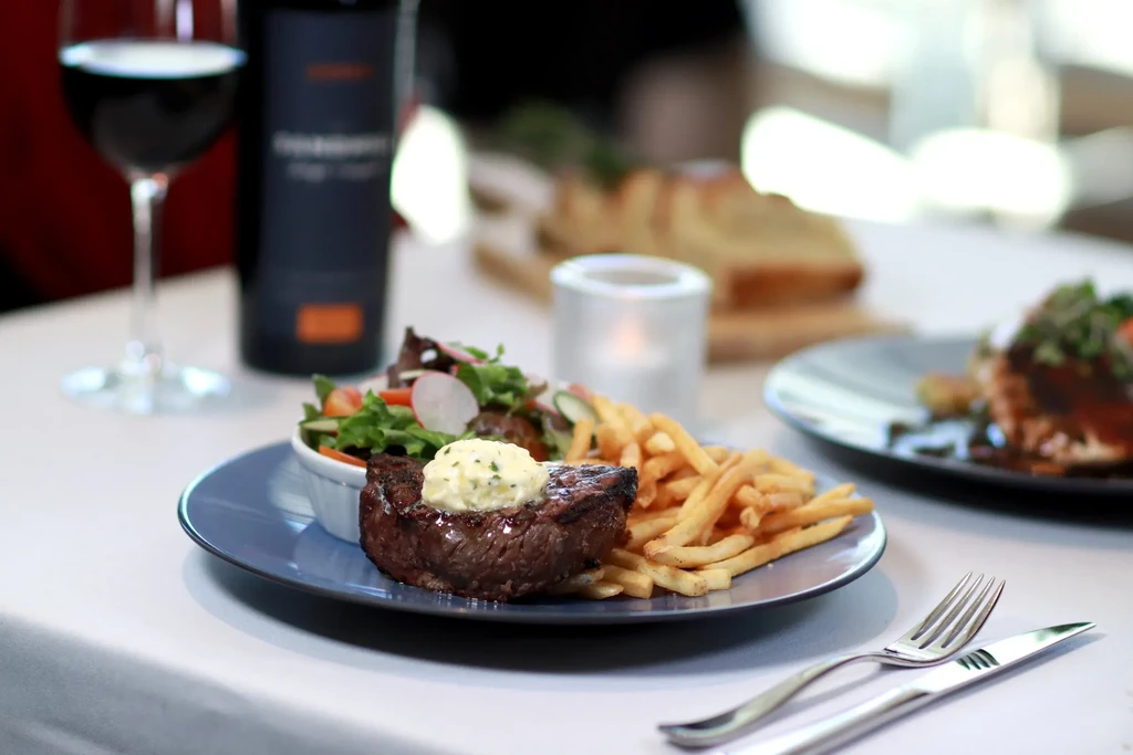 Seared steak with herb butter, french fries, and salad on a blue plate.