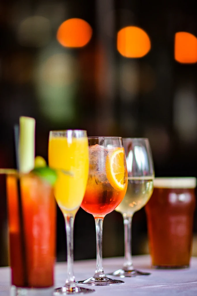 A line of five alcoholic beverages including cocktails, wine, and beer.