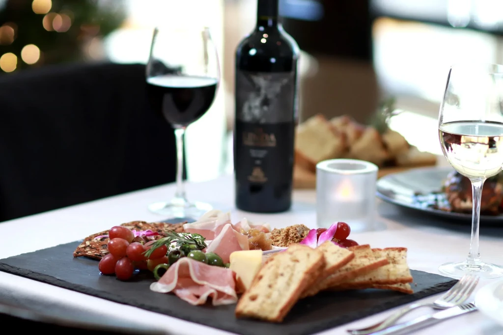 Charcuterie board on slate with meats, cheeses, grapes, wine, and candle.