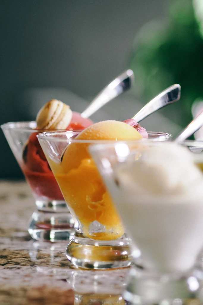 Vibrant orange, pink, and white desserts in glass dishes with spoons.
