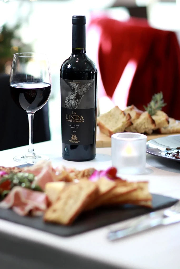 La Linda Malbec, wine glass, and charcuterie board on a restaurant table.
