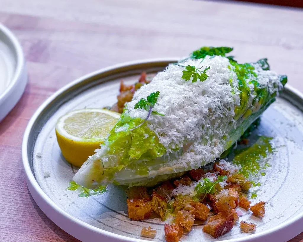Close-up of Caesar salad wedge with grated cheese, croutons, and lemon.