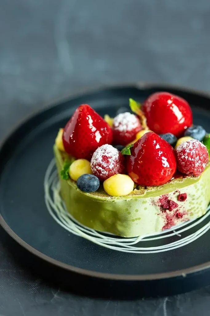 Vibrant green pastry topped with fresh berries, yellow spheres, and white drizzle.