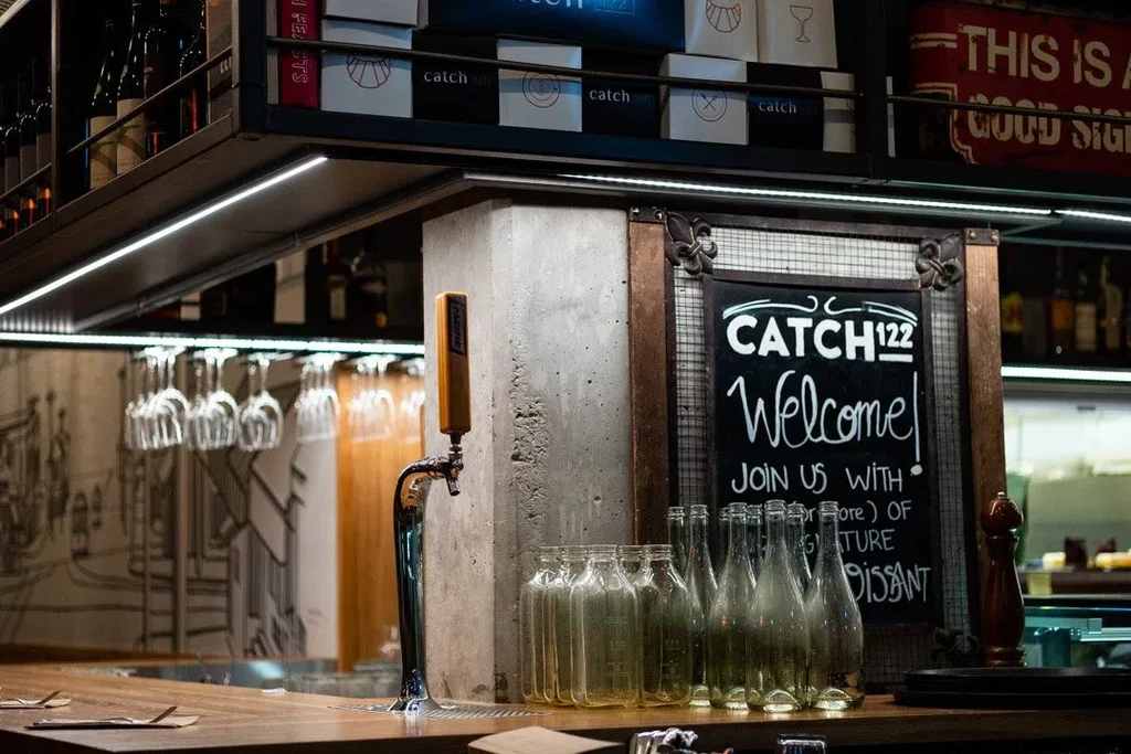 A modern bar counter with beer tap, glass bottles, and chalkboard sign.