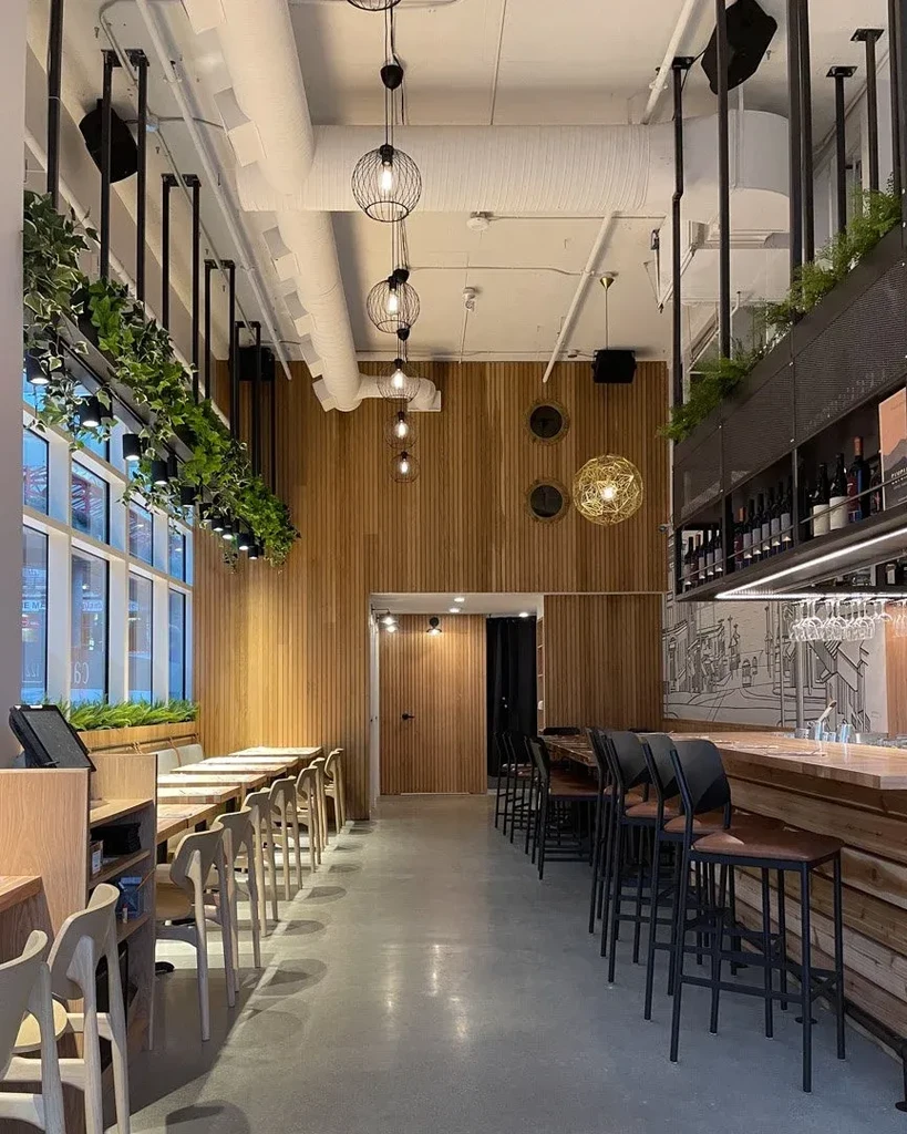 Modern restaurant interior with bar, dining area, hanging plants, and industrial ceiling.